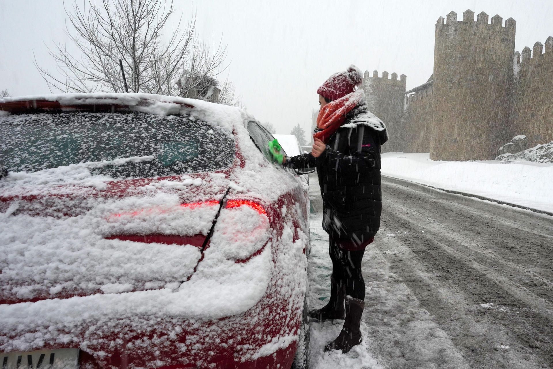 Una persona limpia los cristales de su coche nevado este sábado en Ávila. (EFE/Raúl Sanchidrián)