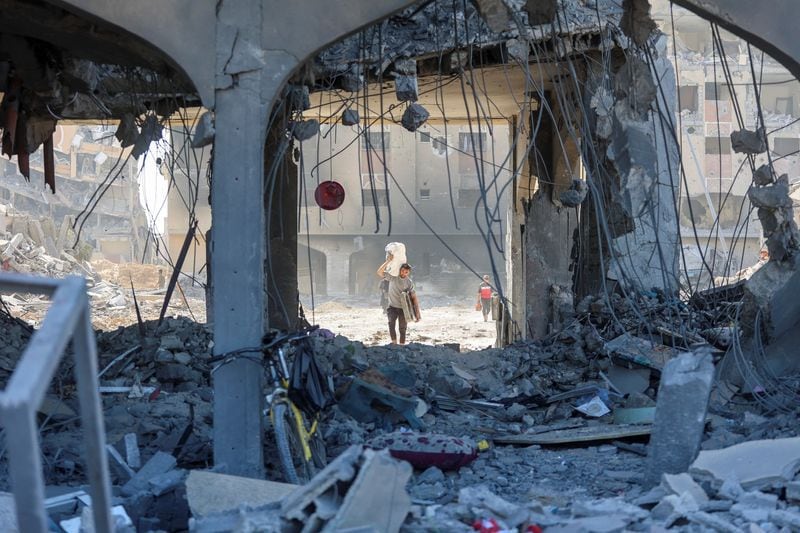 Un hombre palestino lleva sus pertenencias mientras camina entre los escombros de un edificio residencial destruido. REUTERS/Ahmed Zakot/Foto de archivo