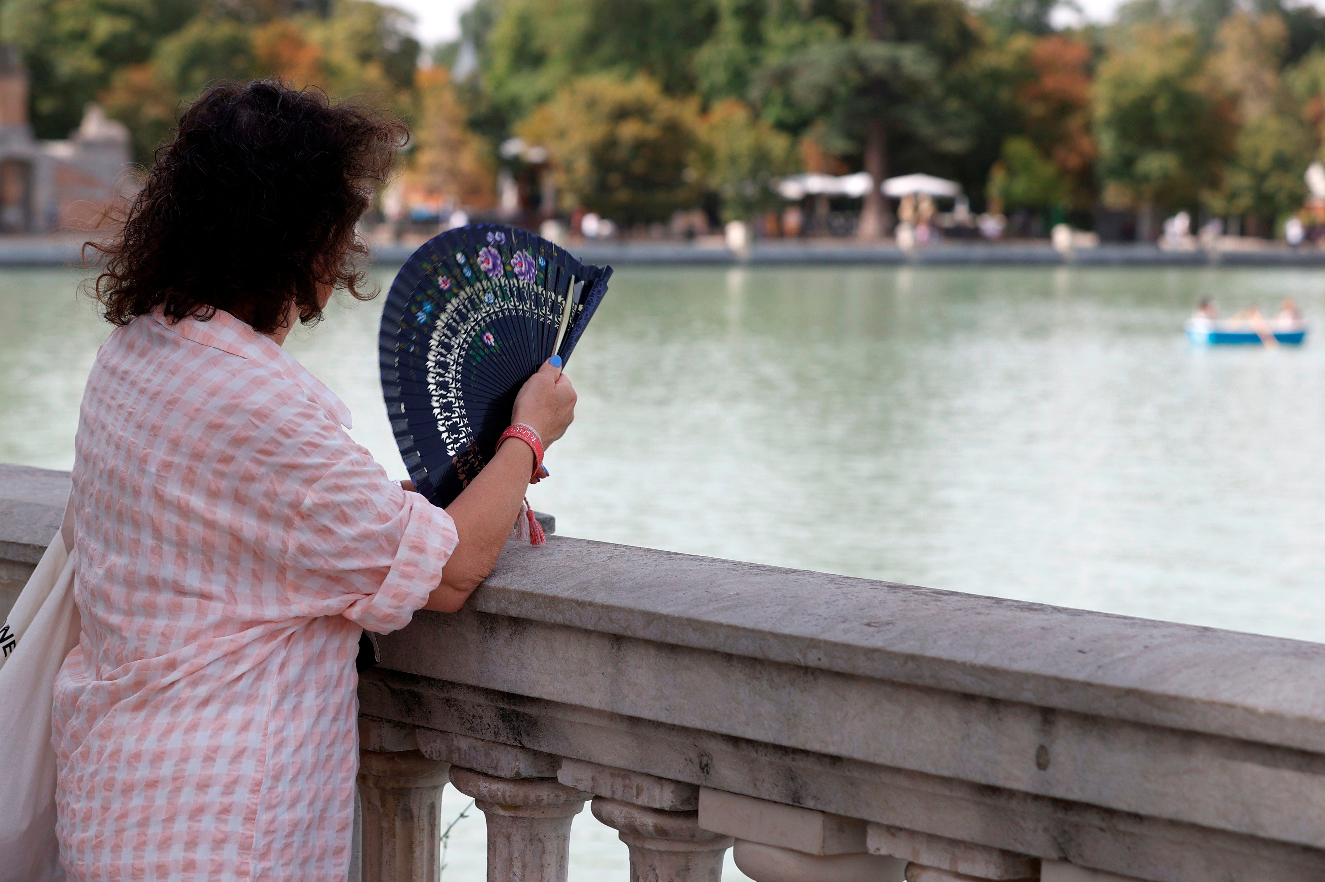 Una mujer combate el calor con un abanico mientras observa el lago del Parque del Retiro de Madrid. (EFE/J.J. Guillén)
