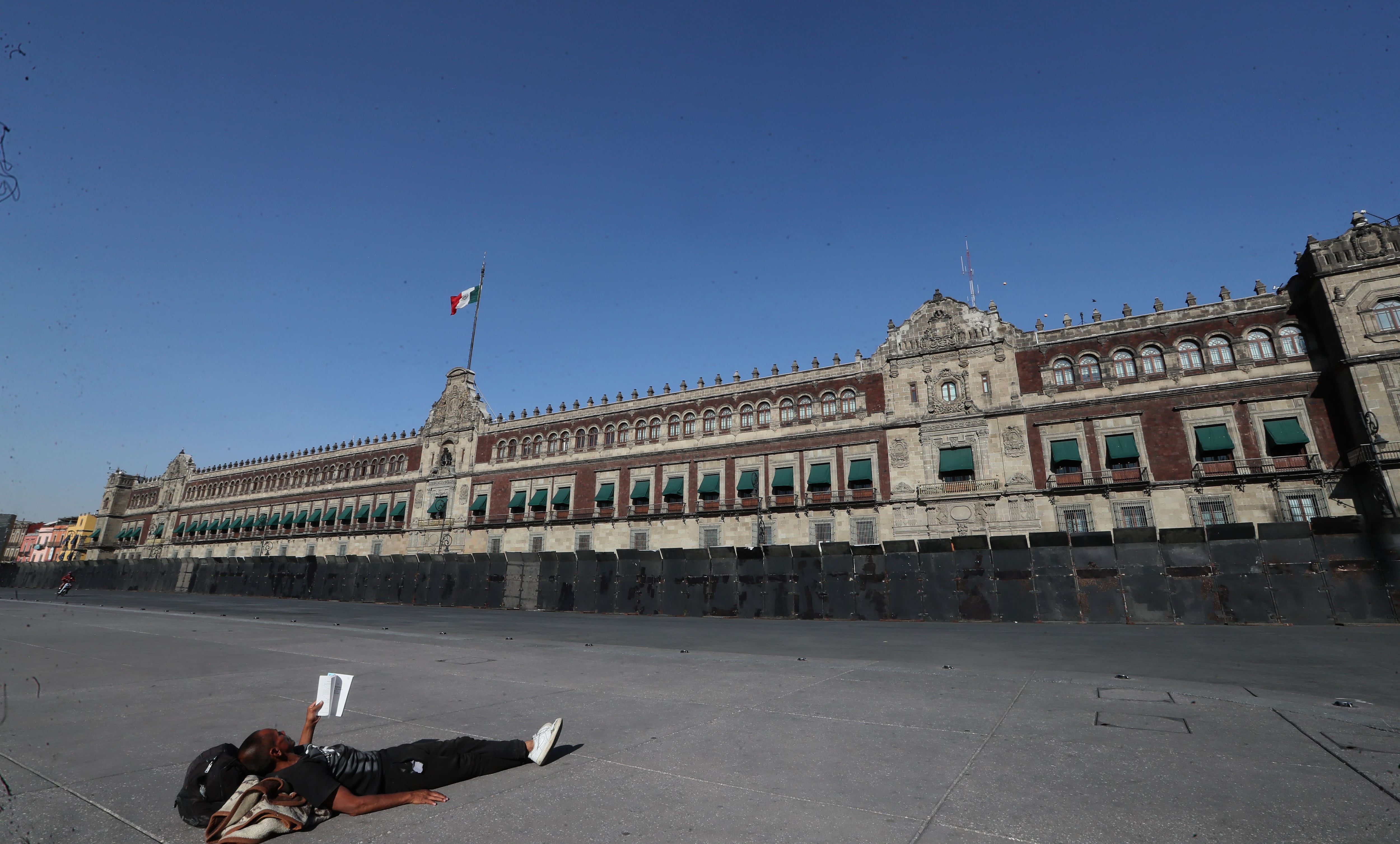 Una persona descansa frente a unas vallas metálicas que rodean el Palacio Nacional este jueves en la Ciudad de México (México). EFE/Mario Guzmán
