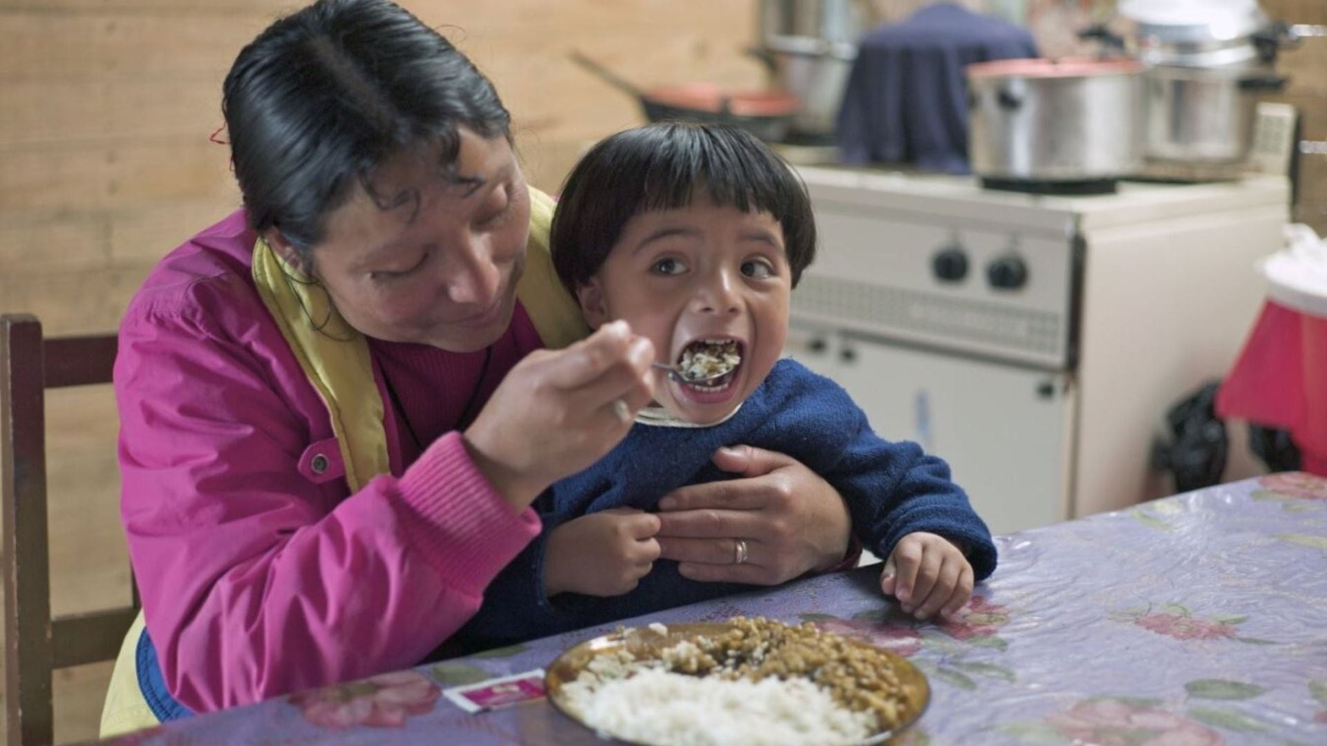 Una madre dando de comer a su hijo un plato de menestras