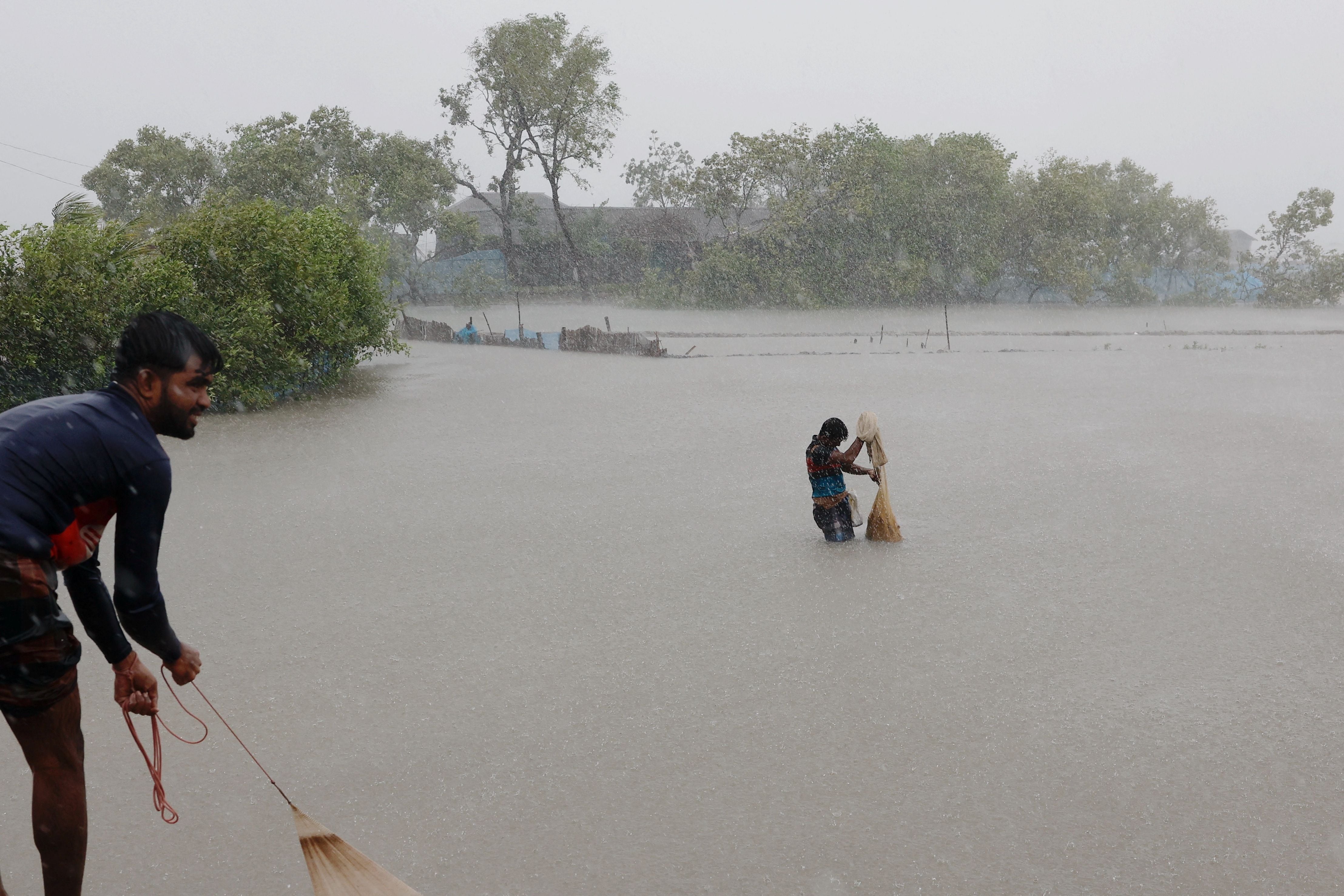 La gente pesca en las granjas de camarones y cangrejos inundadas por las fuertes lluvias (REUTERS/Mohammad Ponir Hossain)