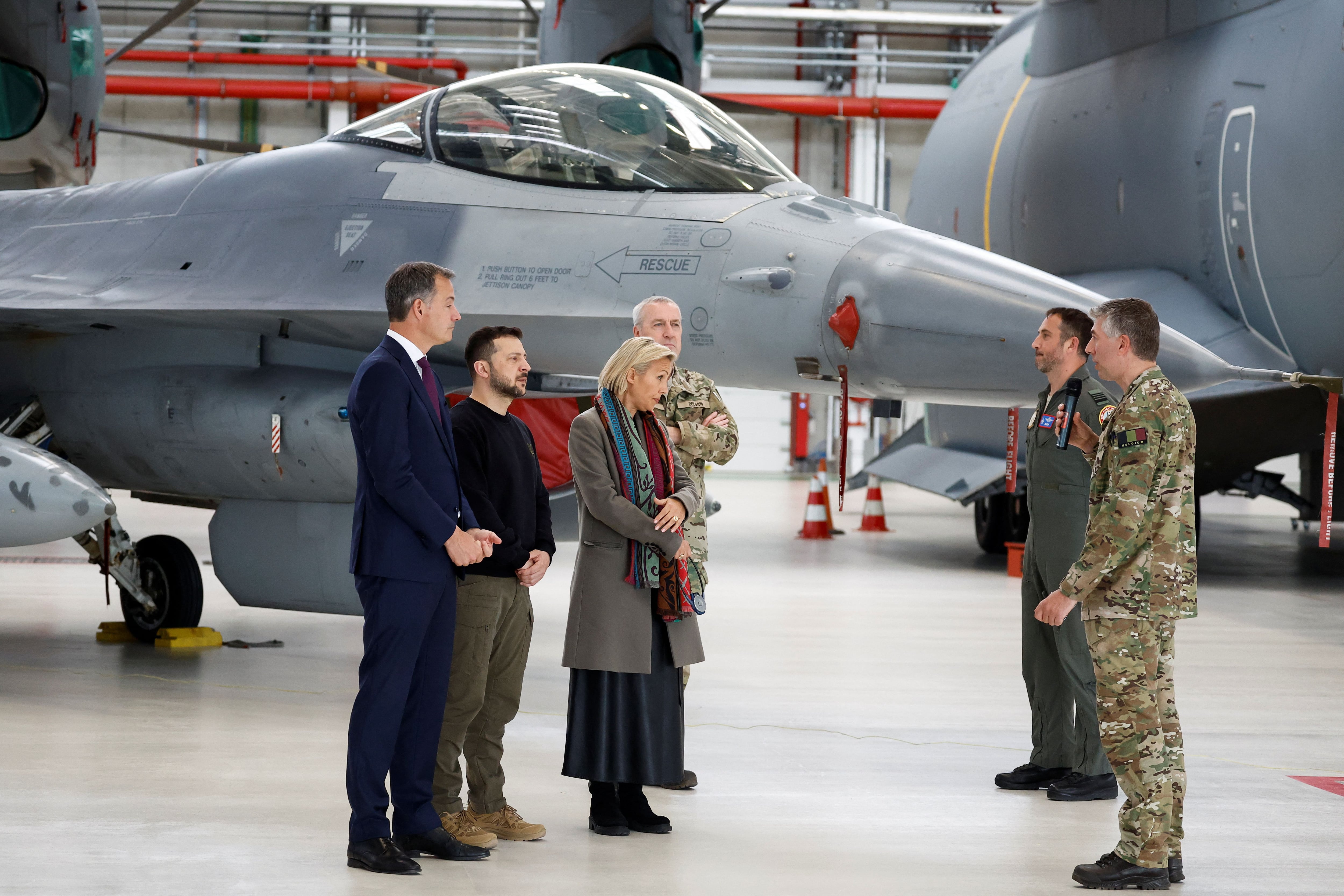 El presidente ucraniano Volodimir Zelensky, el primer ministro belga Alexander De Croo y su ministro de Defensa Ludivine Dedonder dialogan cerca de un avión F-16 junto a instructores de vuelo en la base de Melsbroek (REUTERS/Piroschka van de Wouw)
