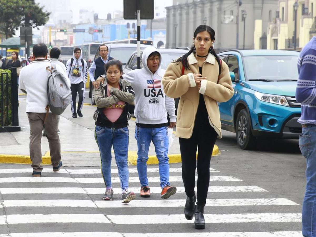 Unos ciudadanos, bien abrigados, se desplazan por una calle del Cercado de Lima, en la capital peruana, en un día frío de otoño.