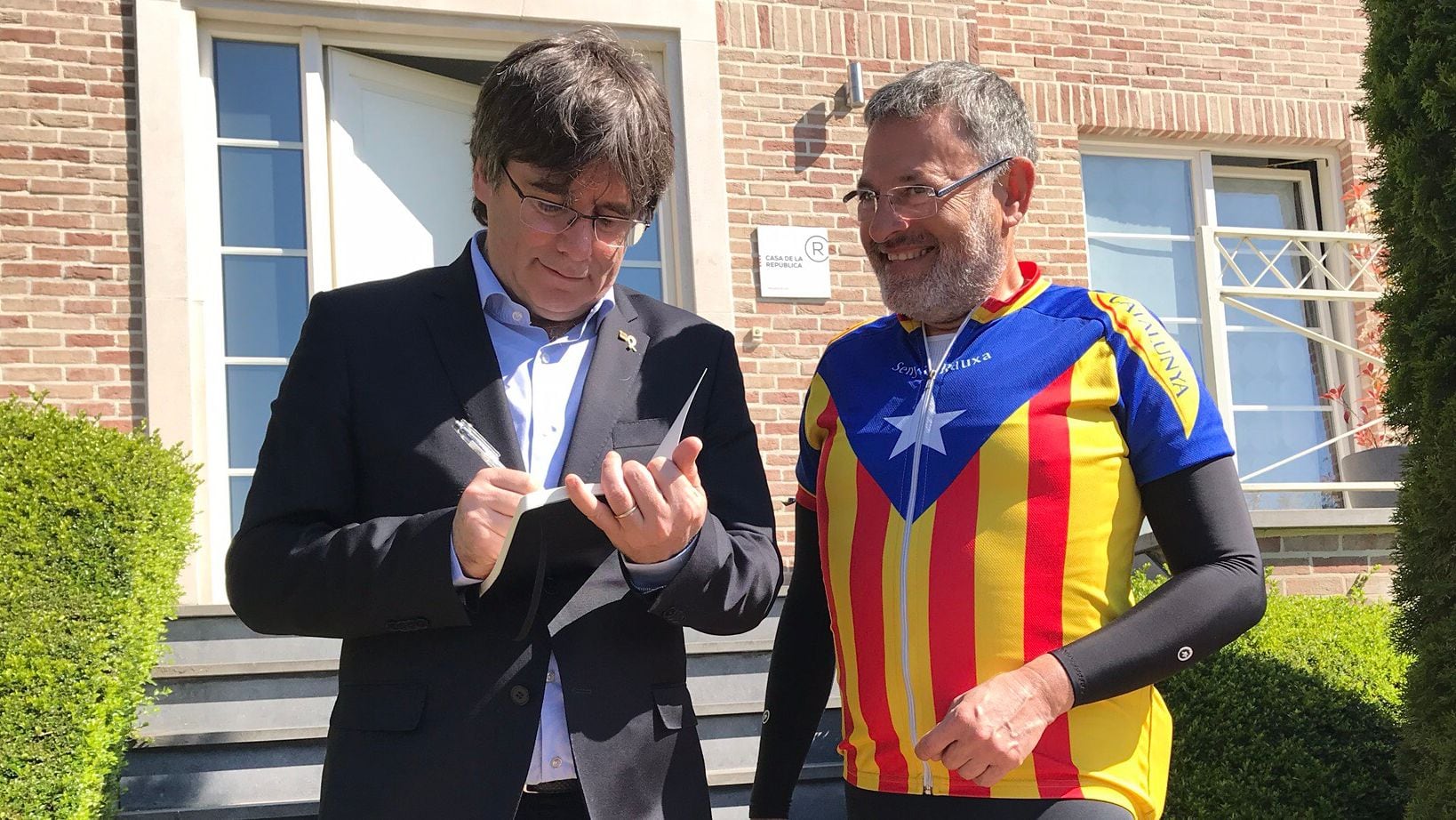 Carles Puigdemont, en su casa de Waterloo, firmando un autógrafo a un fan que porta una bandera independentista como chaqueta. (CASA DE LA REPÚBLICA)